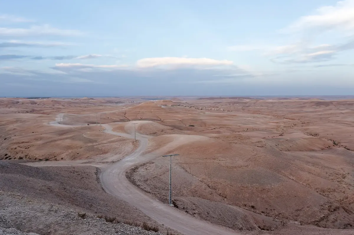 A track winding through the pale, rolling hills of the Agafay Desert at dusk